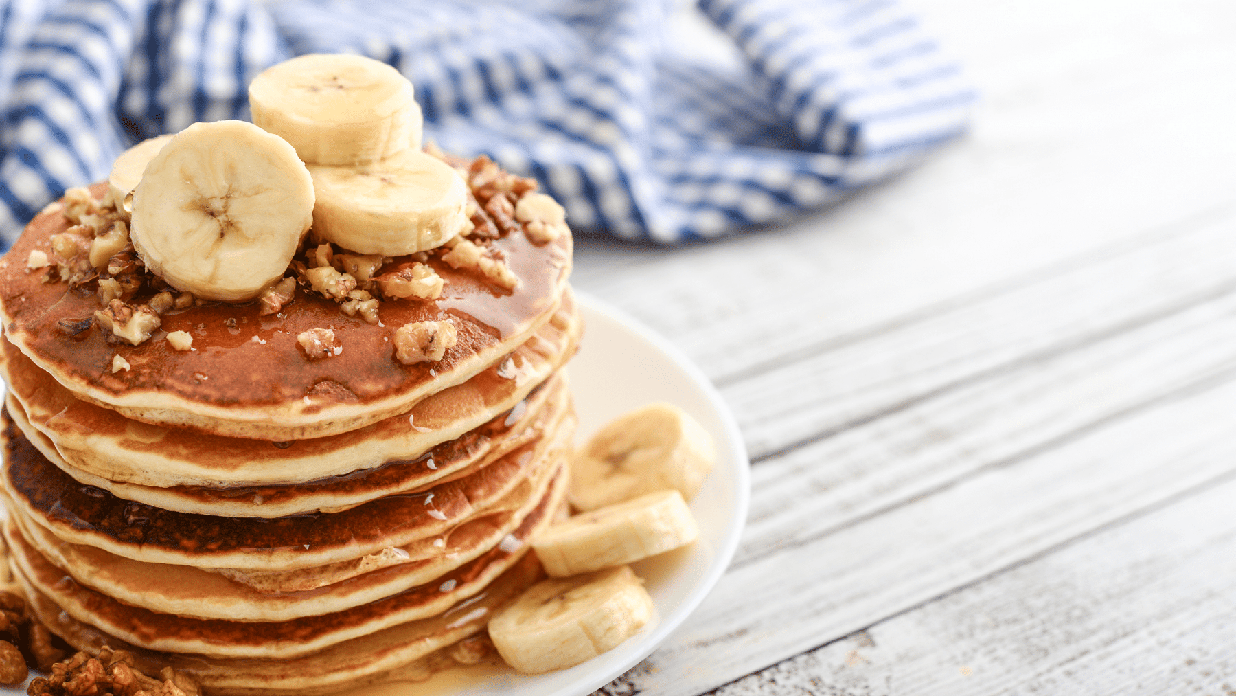 banana pancakes sprinkled with nuts on a wooden table next to a blue and white cloth