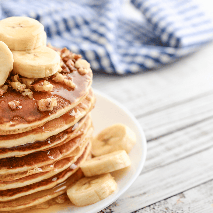 banana pancakes sprinkled with nuts on a wooden table next to a blue and white cloth